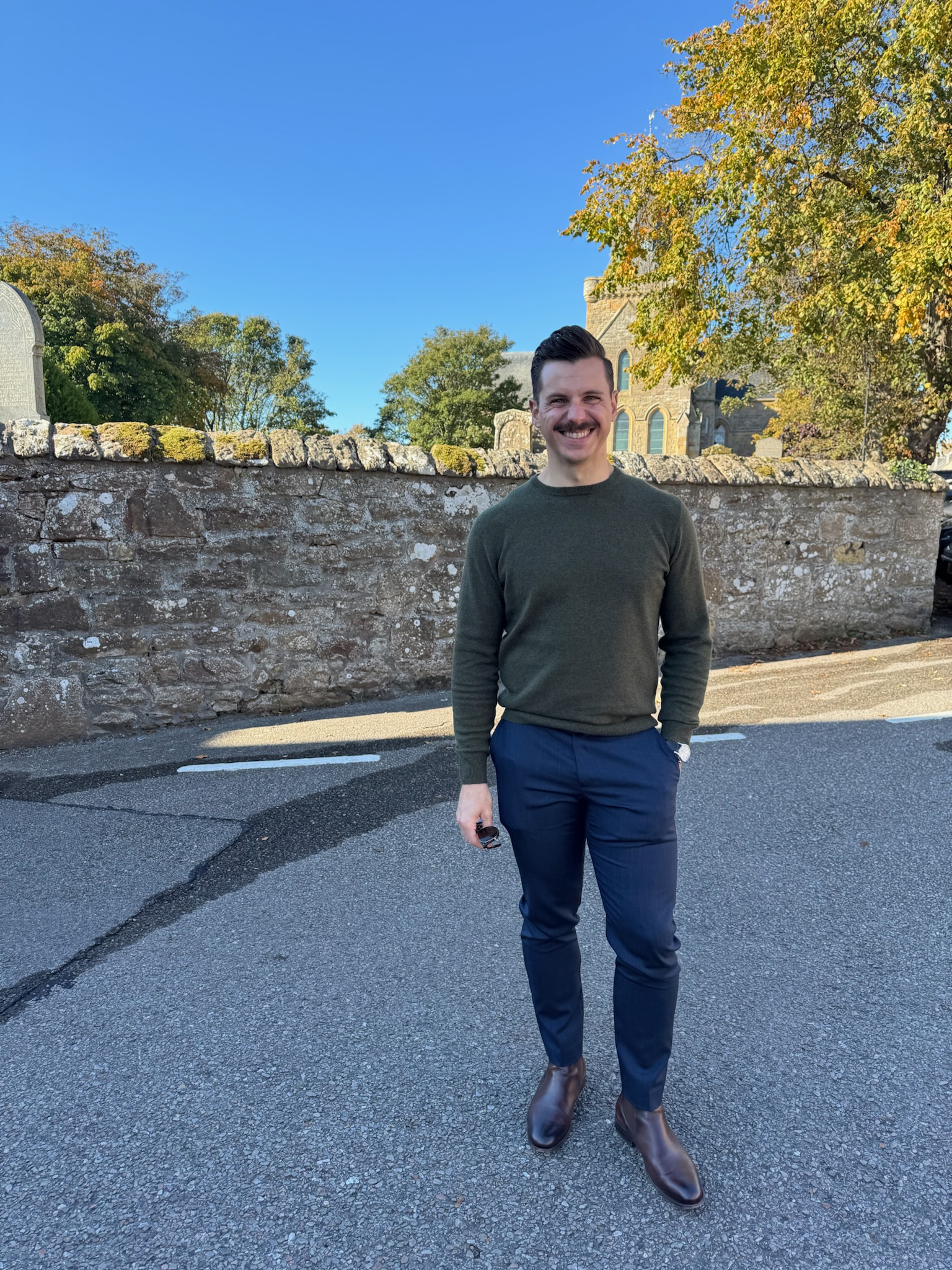 John standing in front of a stone wall surrounding a graveyard in Scotland.
