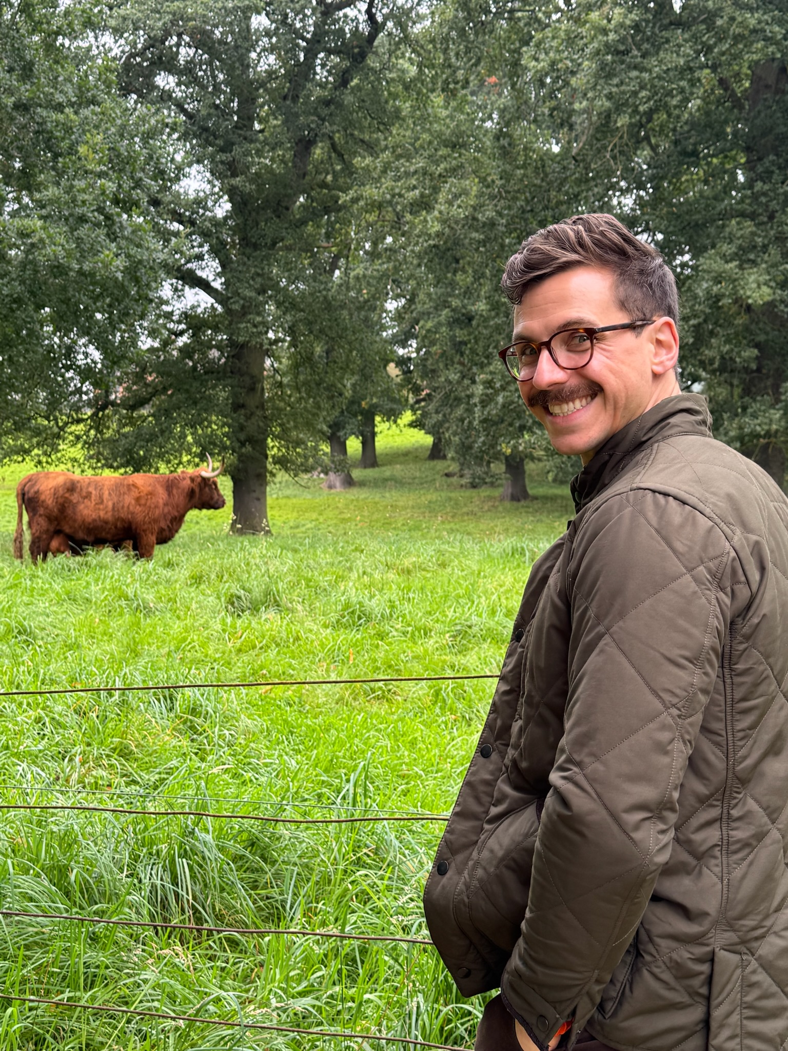 John standing in front of a field with a highland coo grazing.